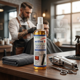 Barber using disinfectant spray to clean scissors and clippers between clients in salon workspace